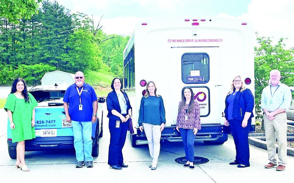 An image of smiling people standing next to UCHRA Public Transportation vehicles including a car and a van.